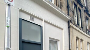 Een gebouw met een donkerblauwe deur, een klein raam en een metalen paal met een bord.