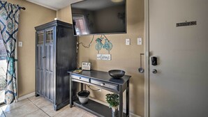 Una habitación con un mueble de madera oscura, una consola con un cuenco y una planta, un televisor montado y una puerta con un letrero de 'No Fumar'.