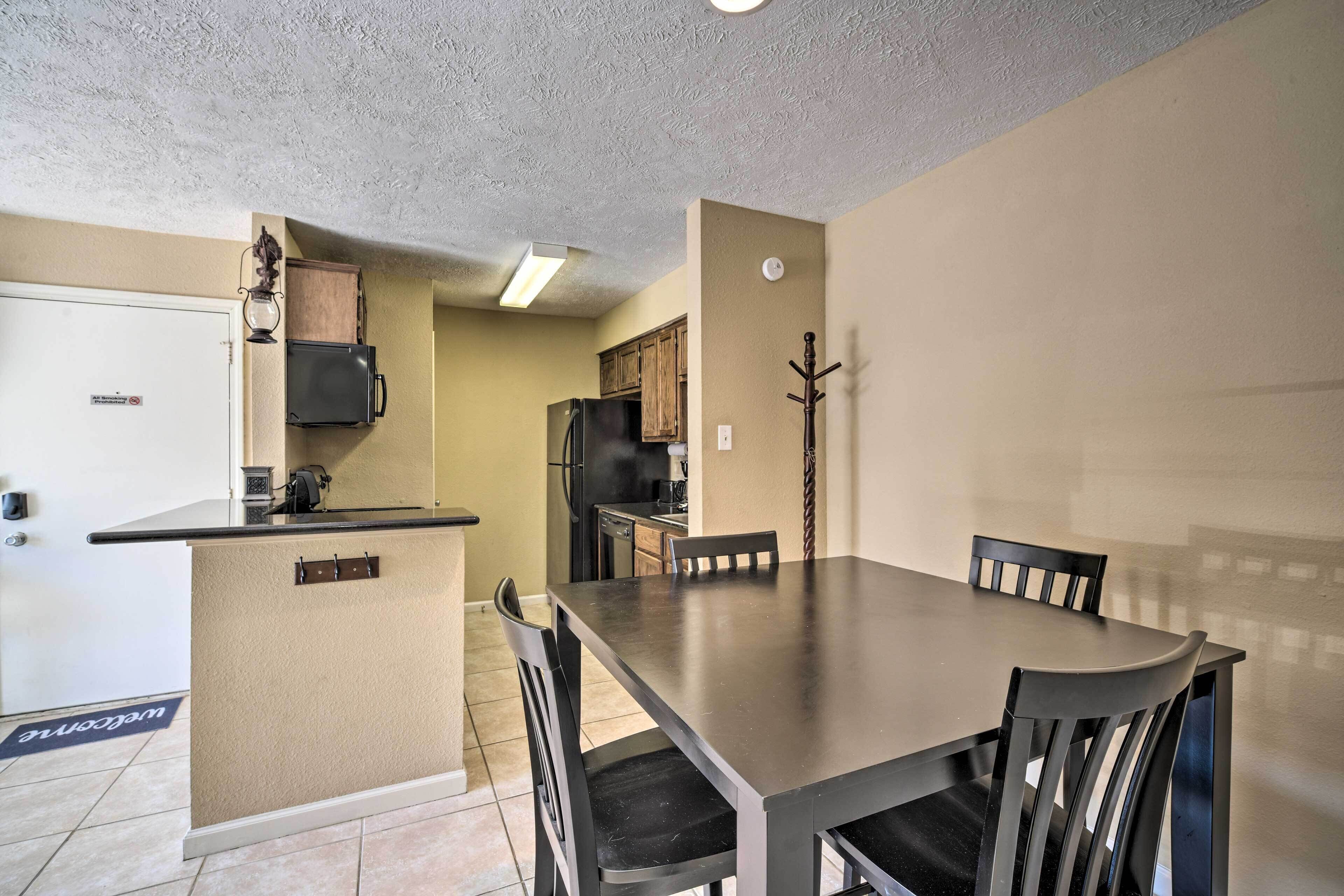 A compact kitchen with a dining area, featuring a central island, dark wooden chairs, and a built-in refrigerator.