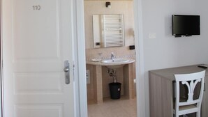 A hotel room with a white door labeled "110", a small bathroom with a sink and mirror, a TV mounted on the wall, and a wooden ceiling beam. - Nebrodi Rooms Monte San Giovanni (San Marco d'Alunzio)