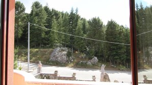 A balcony with a view of a forested area, a stone structure, and a paved road. - Nebrodi Rooms Monte San Giovanni (San Marco d'Alunzio)