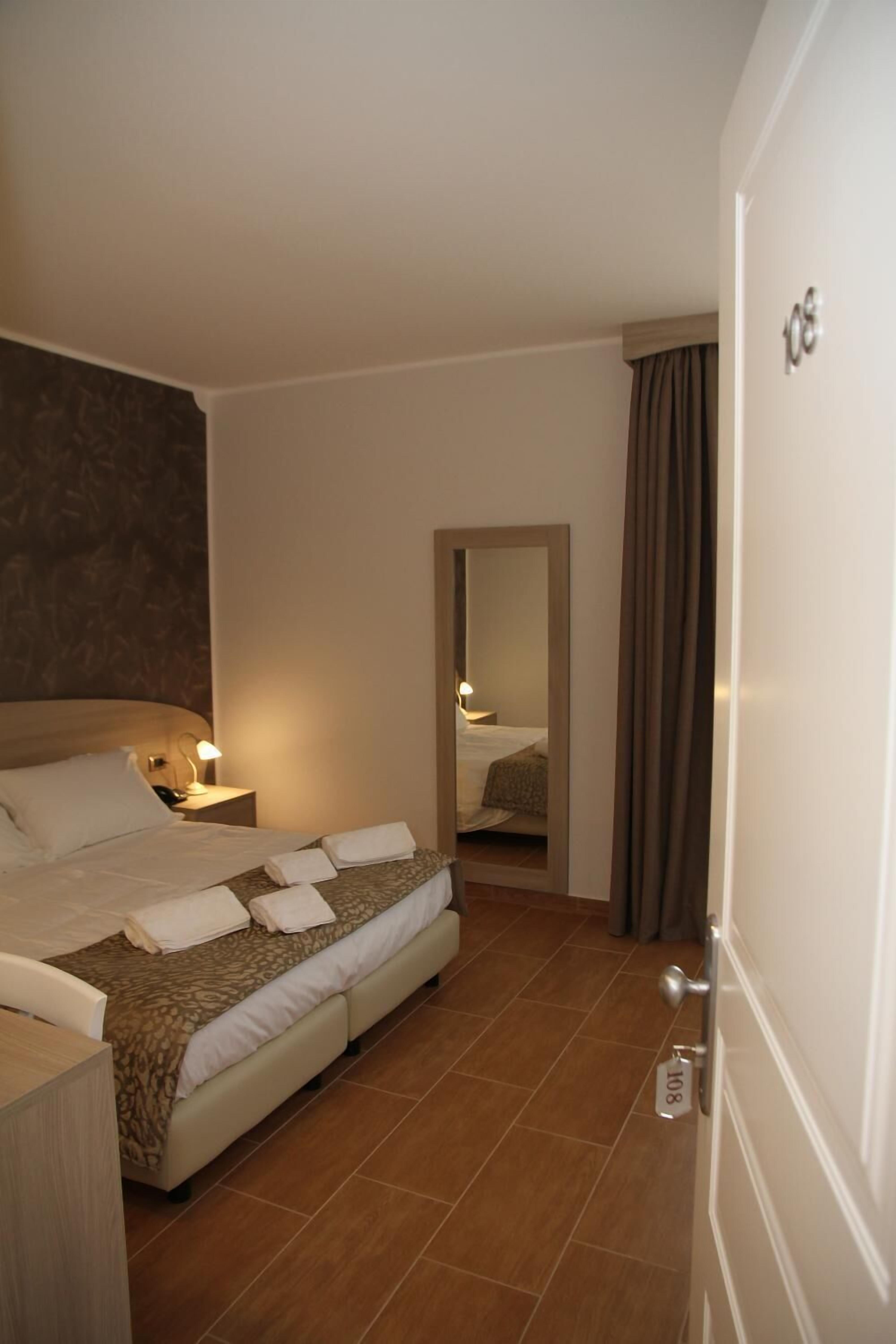 A hotel room with a bed, a nightstand, a mirror, and a door with a number sign.