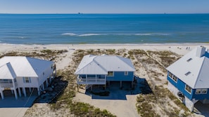 Propiedad frente a la playa con tres casas, cada una con un estilo de techo diferente, ubicada en terreno arenoso con vista al océano.
