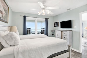 A bedroom with two beds, a ceiling fan, a TV, and a view of the ocean.