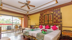 Habitación de hotel con una cama grande, un ventilador de techo, un balcón con vistas a palmeras y un escritorio con lámpara.