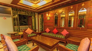 Una habitación tradicional con muebles ornamentados, incluyendo un conjunto de sofás y sillones, una mesa de centro de vidrio y un espejo grande.