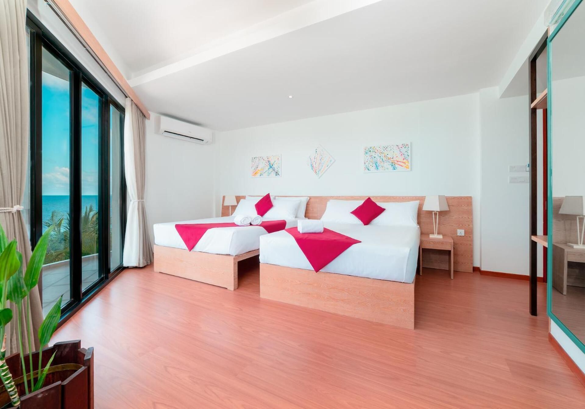 A modern hotel room with two beds, large windows with a view of the sea, and artwork on the walls.