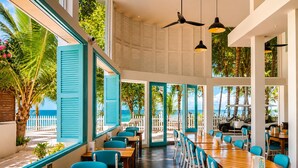A restaurant with large windows, wooden tables, and blue chairs. - Ranthari Hotel and Spa Ukulhas Maldives (Ukulhas)