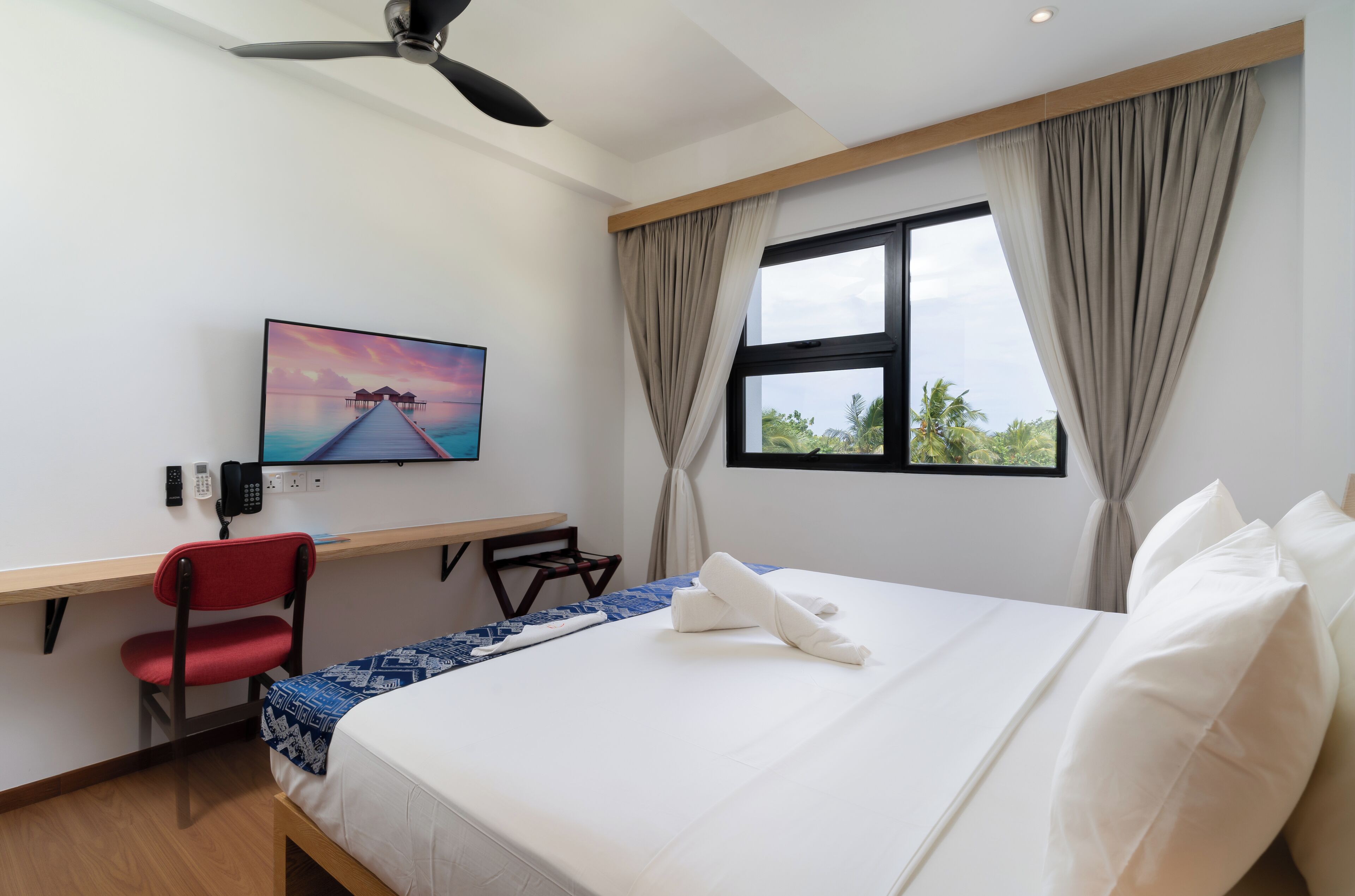 A hotel room with a bed, a desk, a chair, a TV, and a window with curtains.