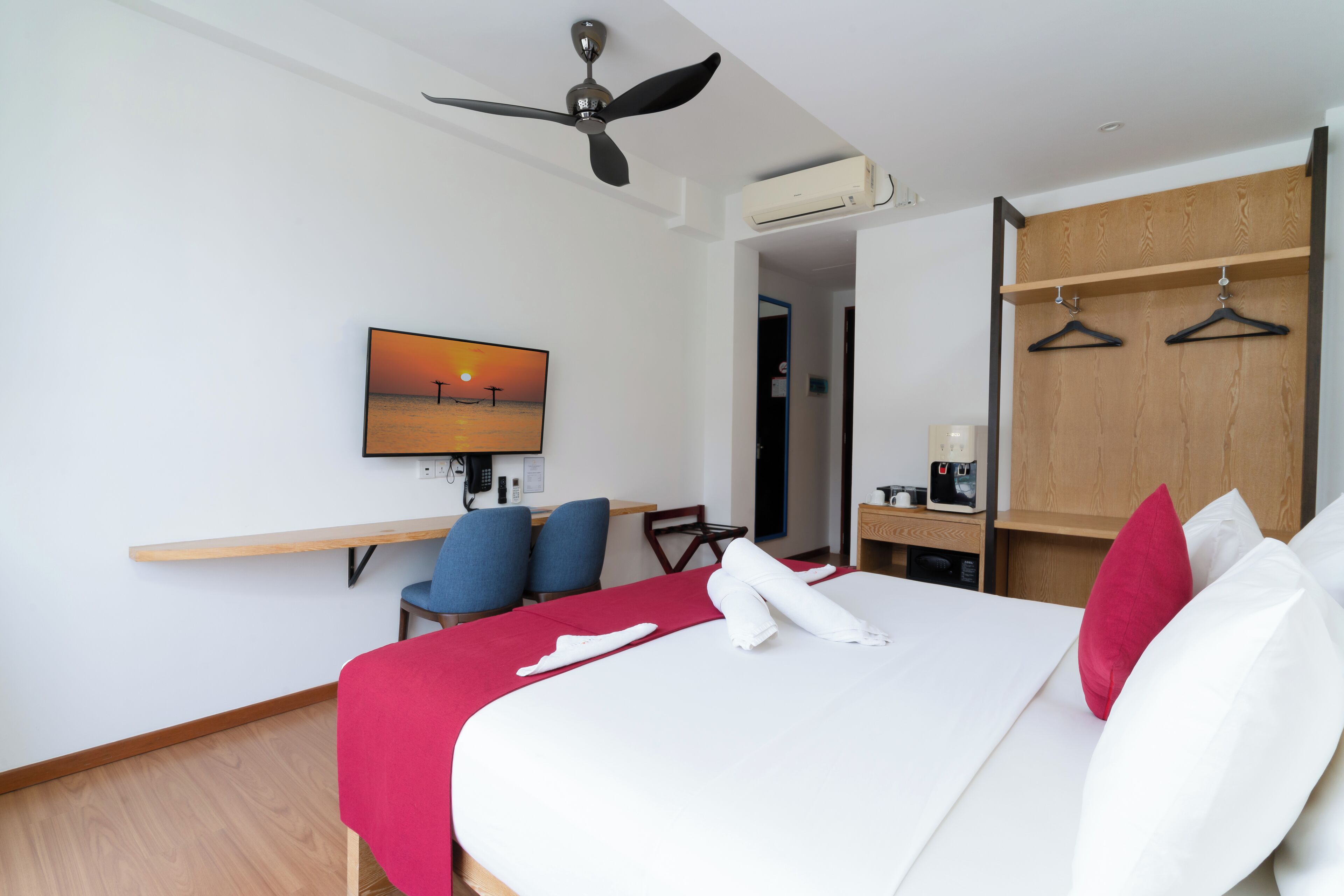 A hotel room with a bed, a desk, a chair, a TV, and a wardrobe.