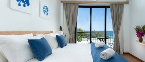 Ein Hotelzimmer mit einem großen Bett, einem Balkon mit Meerblick und Kunstwerken an den Wänden.