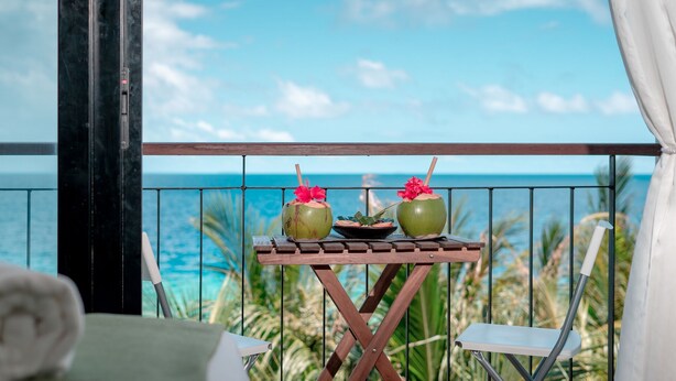 A balcony with a table holding two drinks, a wooden chair, and a view of the ocean. - Ranthari Hotel and Spa Ukulhas Maldives (Ukulhas)