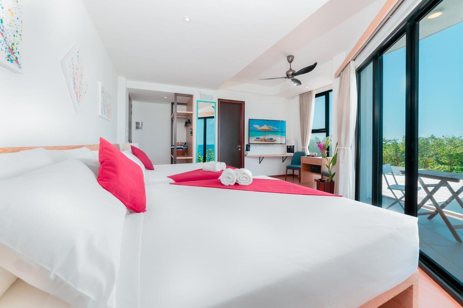 A hotel room with a large bed, a desk, a chair, and a balcony with a view.