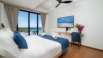 A hotel room with a bed, a desk, a chair, a TV, and a view of the sea.