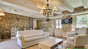 Un salon chaleureux avec un mur en pierre, un canapé à rayures, une table basse blanche et un fauteuil à rayures.