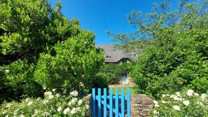 Un sentier qui mène à une maison entourée d’une végétation luxuriante et de fleurs blanches.