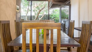 A dining area with wooden tables and chairs, a view of greenery outside, and a wall-mounted picture. - Dollyz Home (Madampagama)