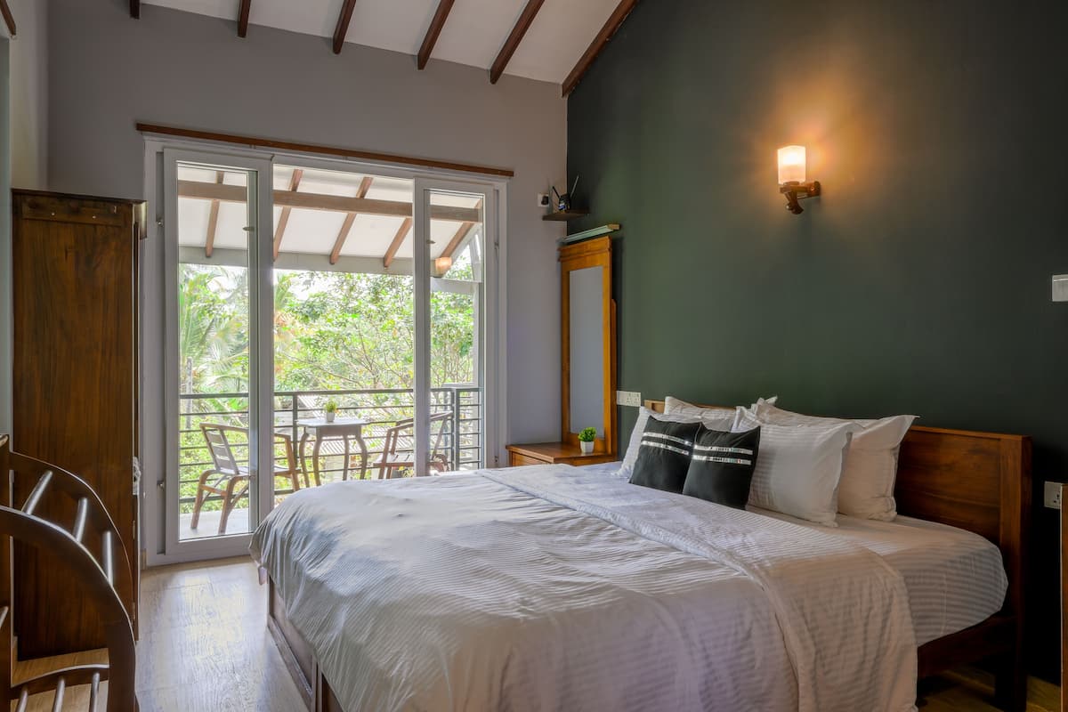 A bedroom with a bed, a nightstand, a mirror, and a sliding glass door leading to an outdoor area with a table and chairs.
