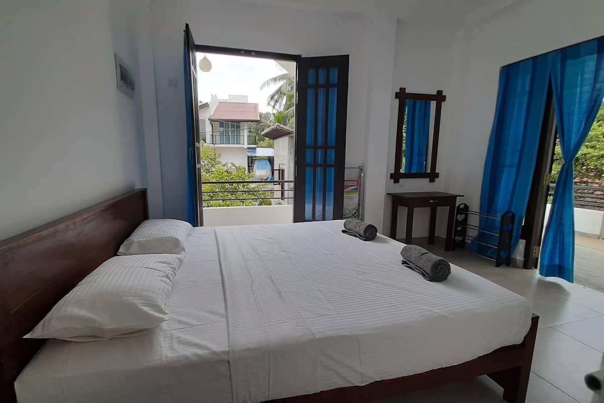 A bedroom with a bed, a small table, and a balcony with blue curtains.