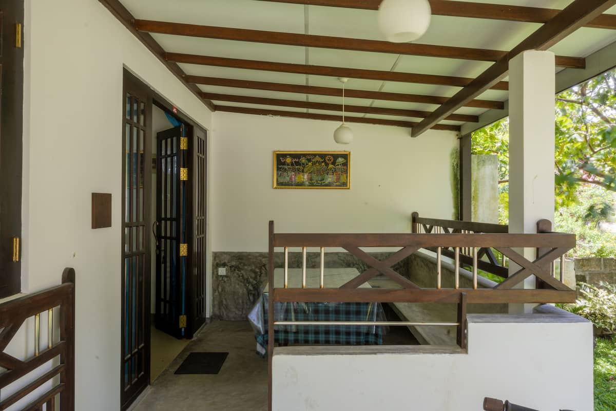 A room with a wooden staircase, a bed with a plaid bedspread, a wall-mounted light fixture, and a door with a decorative gate.