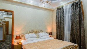 A spacious bedroom with a large bed, a chandelier, and a mirror. - Turan Hotel (Almaty)