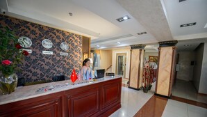 A reception desk with flags, clocks, and a vase of flowers. - Turan Hotel (Almaty)