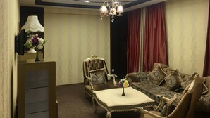A room with a tufted sofa, a round table, a chandelier, and a red curtain. - Turan Hotel (Almaty)