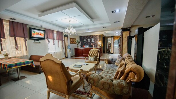 A spacious living room with a large TV, elegant furniture, and a chandelier. - Turan Hotel (Almaty)
