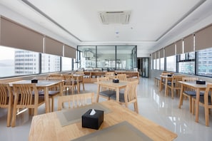 A modern dining area with wooden tables and chairs, large windows, and a view of the city. - XO Hotel & Apartments (Nha Trang)