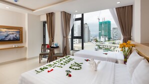 A hotel room with two beds, a TV, a desk, and a view of the cityscape. - XO Hotel & Apartments (Nha Trang)