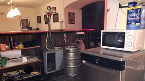 A kitchen with a stainless steel refrigerator, a microwave, and a large gas cylinder. There are shelves with various items, a sink, and a red countertop. - Former Pub 3 for Stag do  men's cave  bachelor, bachelorette party for sleepers (IX. kerület)