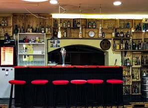 A bar with wooden shelves stocked with liquor bottles, a clock, and red bar stools. - Former Pub 3 for Stag do men's cave bachelor, bachelorette party for sleepers (IX. kerület)