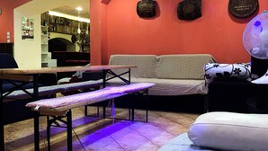 A cozy living area with a sofa, a bench, a table, and a fan. There are decorative plates on the wall and a poster on the wall. - Former Pub 3 for Stag do  men's cave  bachelor, bachelorette party for sleepers (IX. kerület)