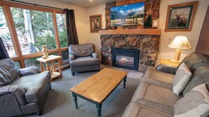 A cozy living room with leather sofas, a wooden coffee table, a stone fireplace, and a large TV mounted on a stone wall. - Free Standing Cabin Nestled in Rocks with Outdoor Hot Tub (Estes Park)