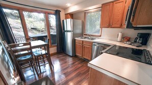 A kitchen with wooden cabinets, a stainless steel refrigerator, a dishwasher, and a black induction cooktop. - Free Standing Cabin Nestled in Rocks with Outdoor Hot Tub (Estes Park)
