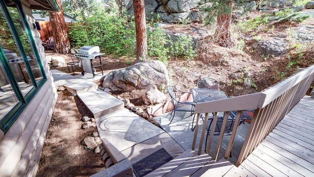 A wooden deck with outdoor furniture, a barbecue grill, and a stone pathway leading to a house. - Free Standing Cabin Nestled in Rocks with Outdoor Hot Tub (Estes Park)