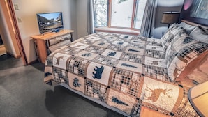 A bedroom with a large bed, a television on a wooden nightstand, a window with curtains, and a lamp on the side table. - 1 Bedroom, 1 Bath, Large Deck with Personal Hot Tub, Grill and Patio Furniture. (Estes Park)