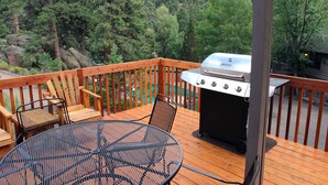 A wooden deck with a grill, a round metal table, and two chairs. - 1 Bedroom, 1 Bath, Large Deck with Personal Hot Tub, Grill and Patio Furniture. (Estes Park)