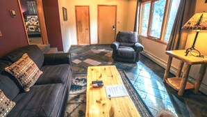 A living room with a leather sofa, a wooden coffee table with remotes, a leather armchair, and a lamp. - 1 Bedroom, 1 Bath, Large Deck with Personal Hot Tub, Grill and Patio Furniture. (Estes Park)