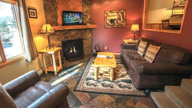 A cozy living room with a fireplace, leather sofa, and a television on a stone wall. - 1 Bedroom, 1 Bath, Large Deck with Personal Hot Tub, Grill and Patio Furniture. (Estes Park)