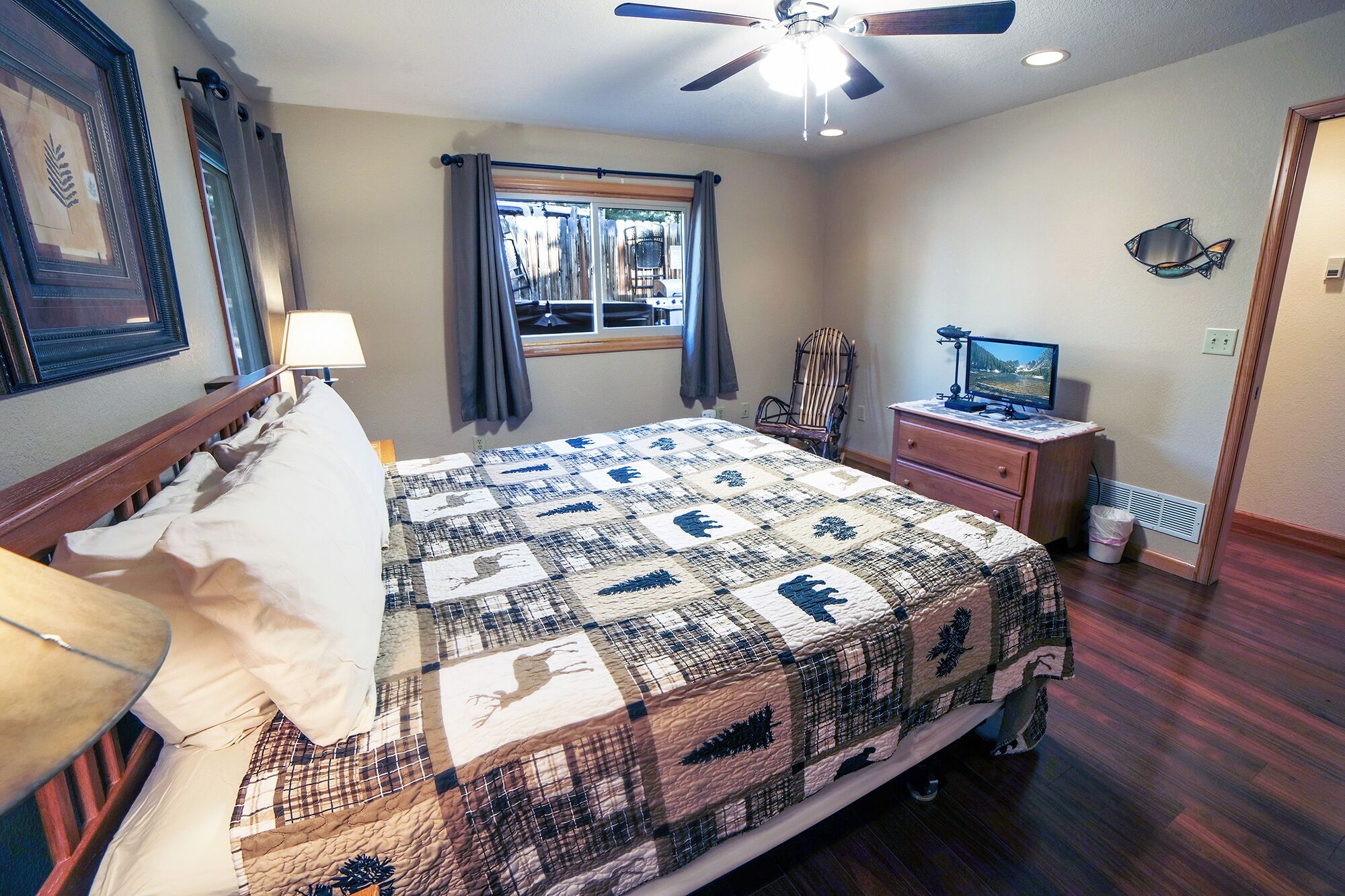 A bedroom with a bed, a desk with a computer, a chair, a window with curtains, and a ceiling fan.