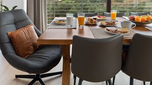 Un comedor con una mesa preparada para el desayuno, vistas al campo y una lámpara de techo moderna.