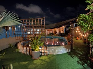A pool area with a wooden deck, potted plants, and string lights.