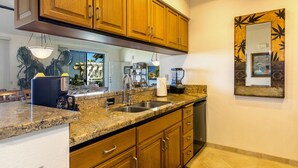 A kitchen with granite countertops, wooden cabinets, a built-in dishwasher, and a large window. - Summer Deal Wailea Ocean View 2BR Condo with Golf Course Access (Kihei)