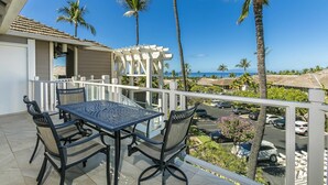 A balcony with a table and chairs, overlooking a parking area and a view of the ocean. - Summer Deal Wailea Ocean View 2BR Condo with Golf Course Access (Kihei)