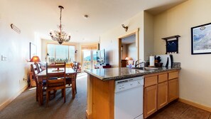 A kitchen with a granite countertop, wooden cabinets, a dishwasher, and a dining area with a table and chairs. - Gorgeous Mountain Décor, Balcony with Views. Near Biking Trails, Pool On-site (Mammoth Lakes)