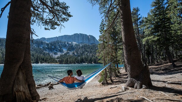 A hammock between two trees overlooking a lake with mountains in the background. - Gorgeous Mountain Décor, Balcony with Views. Near Biking Trails, Pool On-site (Mammoth Lakes)