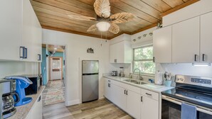 Cocina moderna con armarios blancos, refrigerador de acero inoxidable, horno empotrado y ventilador de techo.