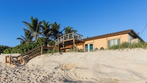 A beachfront property with a wooden staircase leading to a deck, surrounded by palm trees and a sandy beach. - Private Beach Access- Direct Oceanfront (Melbourne Beach)