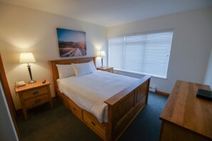 A hotel room with a single bed, bedside tables with lamps, a desk, and a window with blinds. - Stoney Creek Northstar 6 (Whistler)